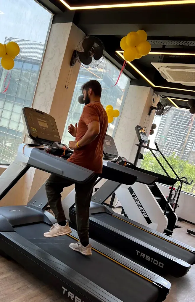 A member walking on a treadmill beside full-height windows looking out over Noida